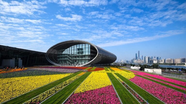 The exterior of the Canton Fair Complex surrounded by vibrant flower gardens, showcasing Guangzhou’s nickname as the "Flower City.
