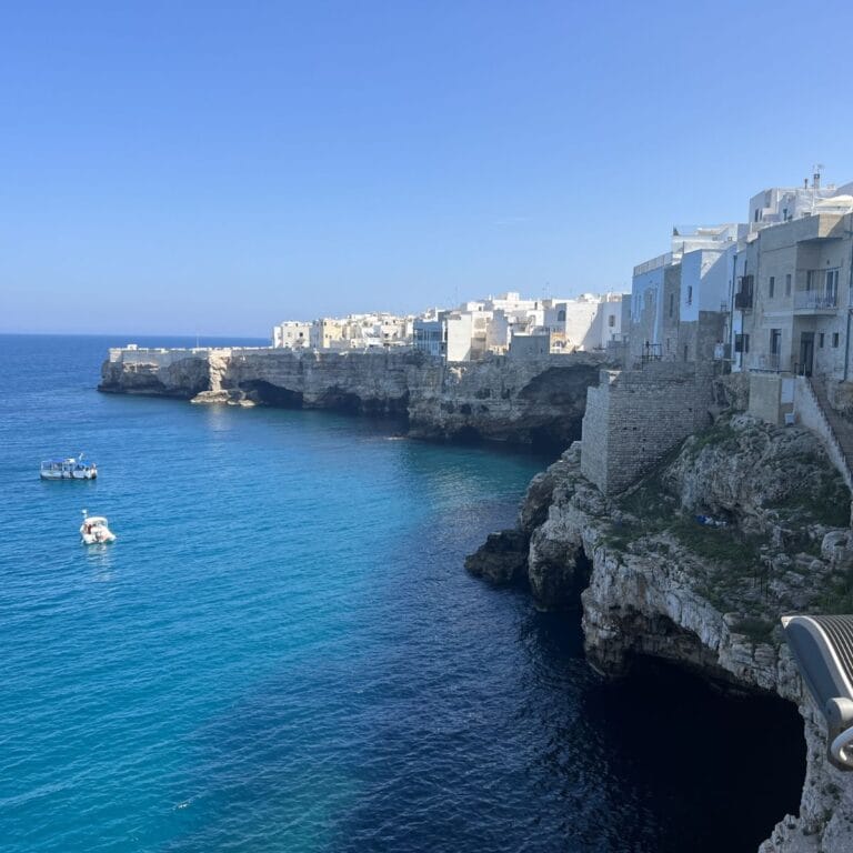 A breathtaking view of Polignano a Mare’s Old Town, where limestone cliffs rise dramatically from the deep blue sea, supporting colorful houses and offering stunning coastal vistas.