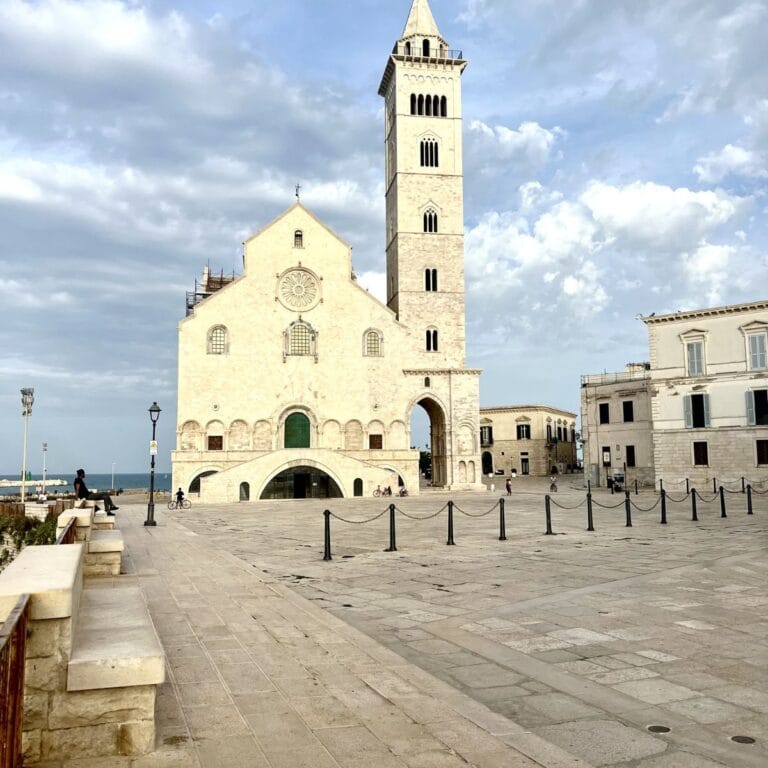 Trani Cathedral, a Romanesque masterpiece perched by the Adriatic Sea, featuring its striking white stone façade, towering bell tower, and intricate rose window.
