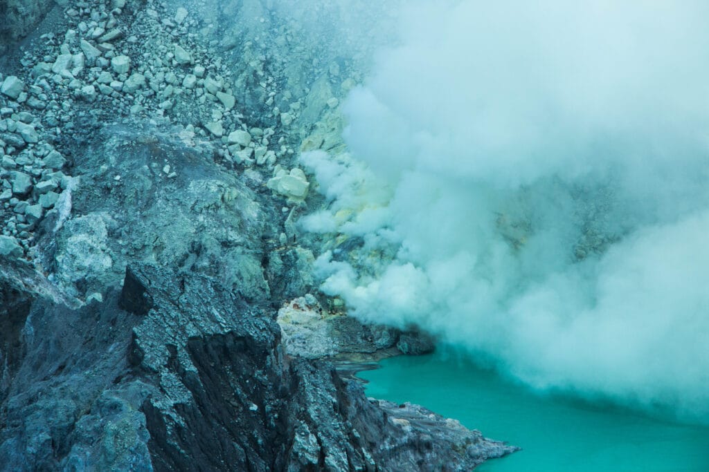 The turquoise crater lake of Kawah Ijen illuminated by sunrise, surrounded by volcanic cliffs and sulphuric smoke