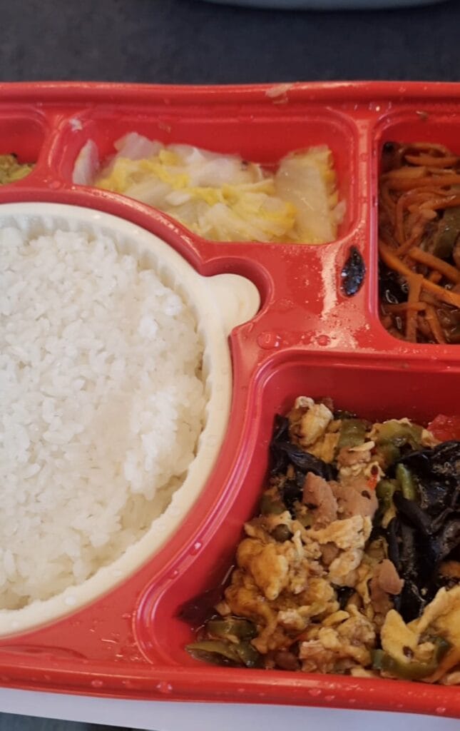 business class meal on Chinese bullet train with multiple Chinese dishes, steamed rice, soup, and beverage on a tray