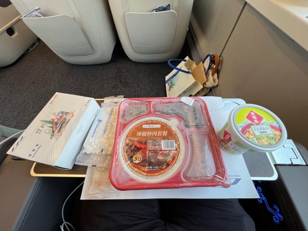 Business class meal set on China high-speed train featuring rice, vegetables, meat dishes, soup, and drink
