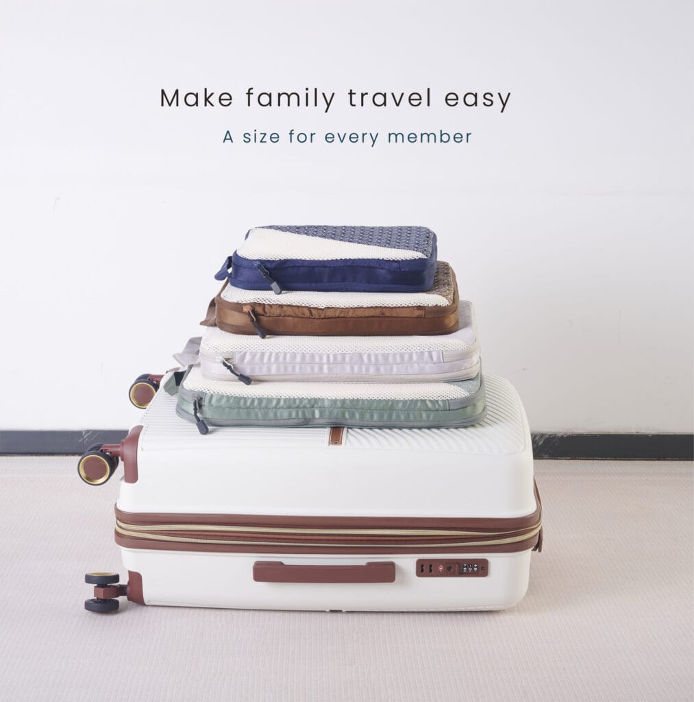 Four Caveri compression packing cubes in different sizes and colours, neatly stacked on top of a closed suitcase.