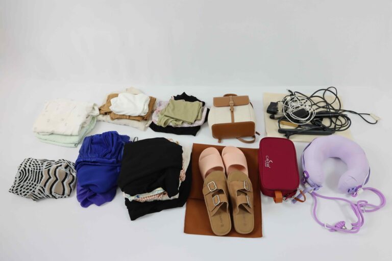 Flat lay of folded clothes, shoes, toiletry bag, tech cables, and a travel pillow